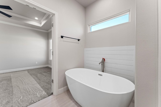 bathroom with a raised ceiling, crown molding, a tub, and ceiling fan