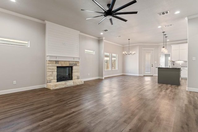 unfurnished living room with crown molding, a stone fireplace, ceiling fan with notable chandelier, and dark hardwood / wood-style floors