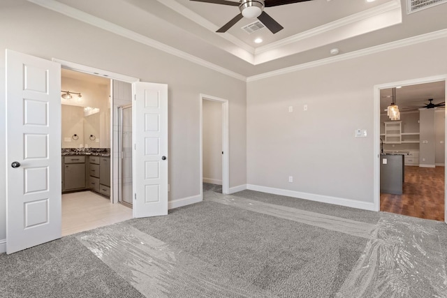 unfurnished bedroom featuring crown molding, ensuite bath, ceiling fan, a tray ceiling, and light colored carpet