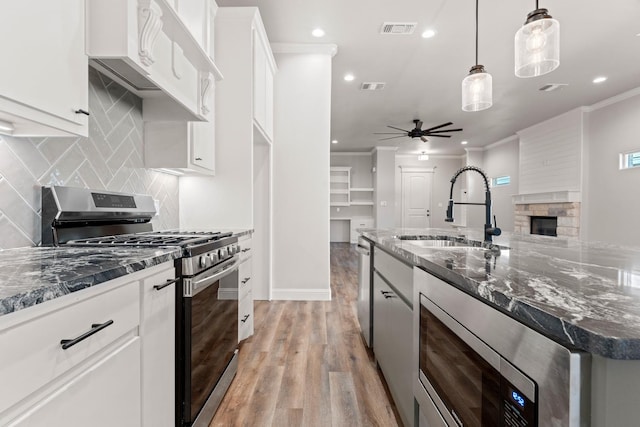 kitchen with sink, white cabinetry, hanging light fixtures, appliances with stainless steel finishes, and dark stone counters