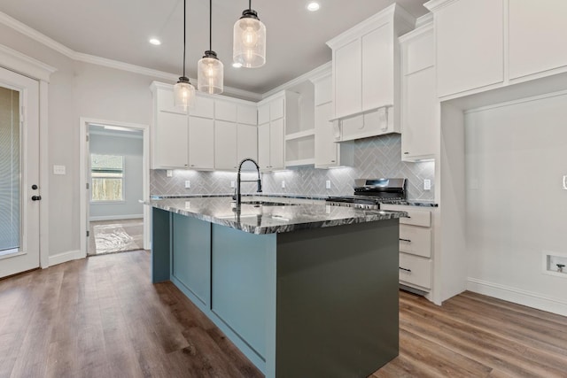 kitchen featuring decorative light fixtures, white cabinetry, sink, a kitchen island with sink, and range