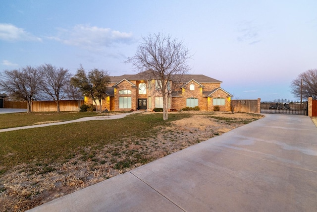view of front of home featuring a gate, concrete driveway, a lawn, fence, and brick siding