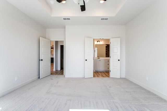 unfurnished bedroom with ceiling fan, light colored carpet, connected bathroom, and a raised ceiling