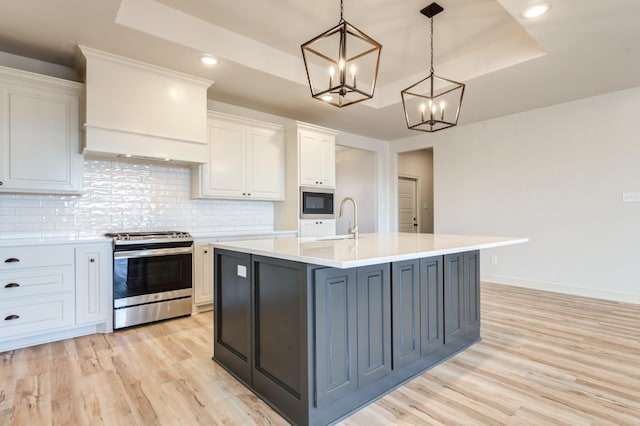 kitchen featuring stainless steel gas stove, a tray ceiling, a kitchen island with sink, and white cabinets