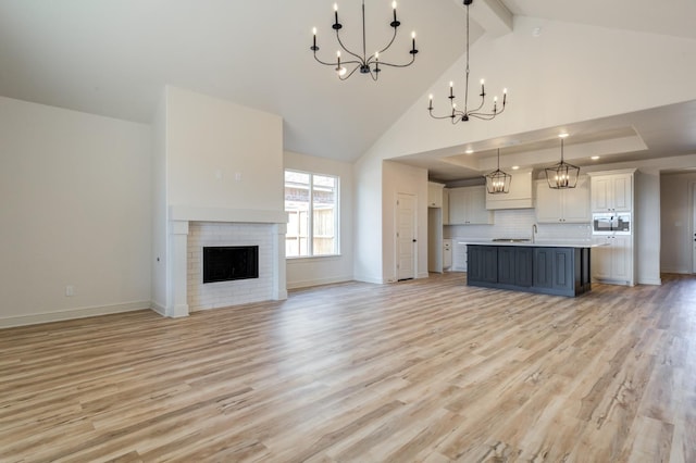 unfurnished living room featuring high vaulted ceiling, beamed ceiling, a notable chandelier, light hardwood / wood-style floors, and a brick fireplace