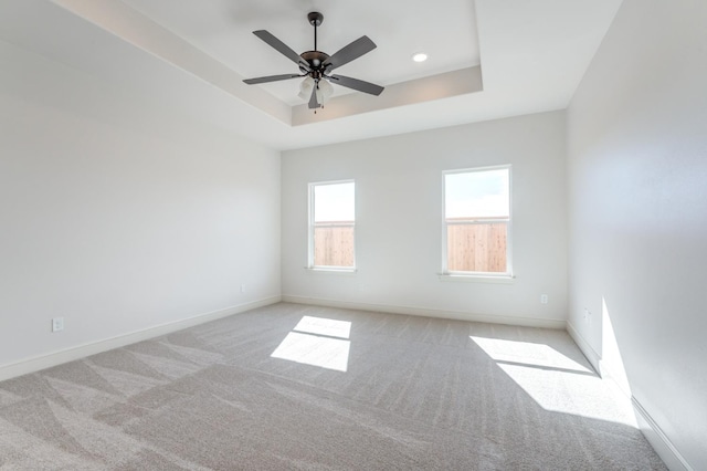 empty room with light carpet, a raised ceiling, and ceiling fan