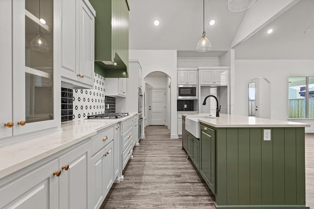 kitchen with appliances with stainless steel finishes, white cabinetry, sink, a kitchen island with sink, and wall chimney range hood