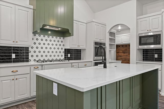 kitchen featuring built in microwave, stainless steel gas cooktop, a center island with sink, light stone countertops, and white cabinets