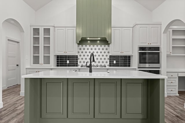 kitchen with white cabinetry, a kitchen island with sink, lofted ceiling, and light hardwood / wood-style flooring