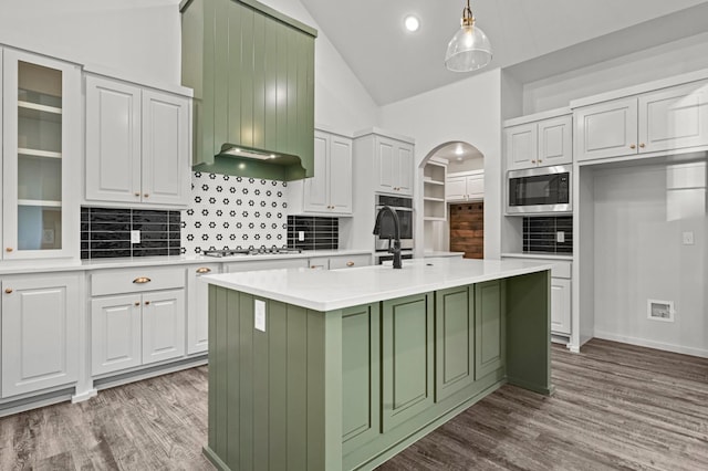 kitchen with white cabinetry, decorative light fixtures, stainless steel microwave, and a kitchen island with sink