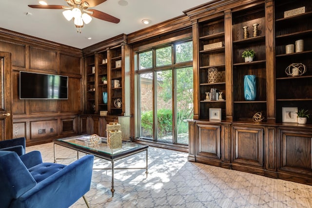 sitting room featuring built in shelves, ceiling fan, and wood walls