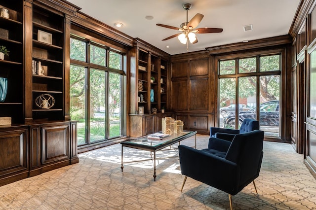 sitting room with crown molding, built in shelves, a wealth of natural light, and wood walls