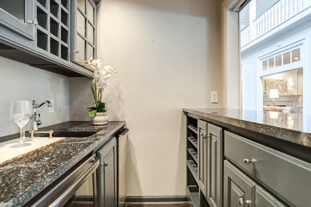 bar with dishwashing machine, sink, gray cabinets, and dark stone countertops