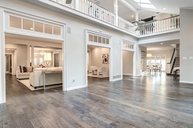 living room with a skylight, ornamental molding, dark hardwood / wood-style flooring, a towering ceiling, and ceiling fan