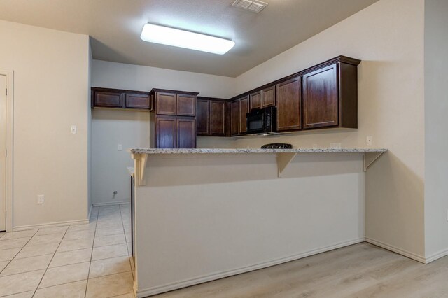 kitchen featuring dark brown cabinetry, a breakfast bar, kitchen peninsula, light stone countertops, and light hardwood / wood-style flooring