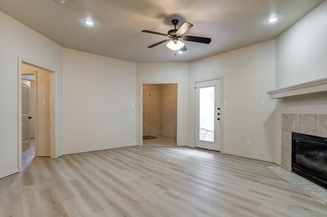 unfurnished living room with ceiling fan, a tiled fireplace, and light wood-type flooring