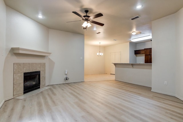 unfurnished living room featuring a fireplace, ceiling fan with notable chandelier, and light wood-type flooring