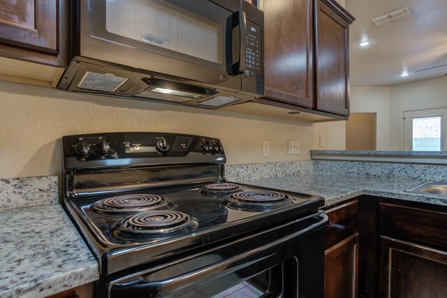 kitchen with dark brown cabinetry, black appliances, and light stone counters