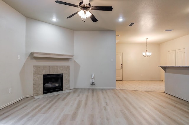 unfurnished living room featuring ceiling fan, a tiled fireplace, and light wood-type flooring