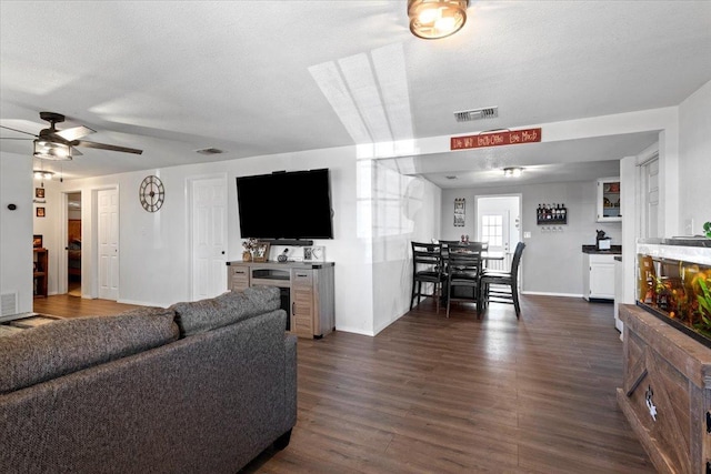 living room with ceiling fan, dark wood-type flooring, and a textured ceiling