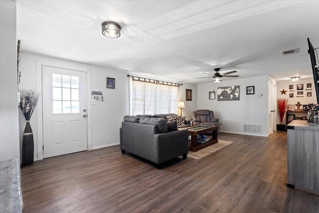 living room featuring dark wood-type flooring, ceiling fan, and a textured ceiling