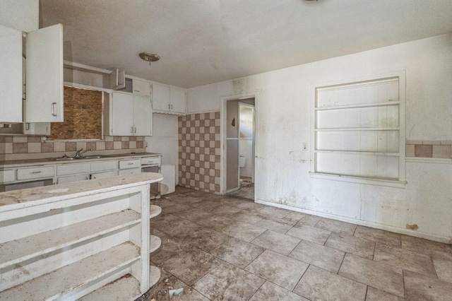 kitchen with white cabinetry, dishwashing machine, sink, and backsplash