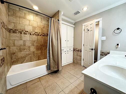 5712 70th Pl, Lubbock, TX 79424 - bathroom with crown molding, tile patterned floors, shower / tub combo, tile walls, and double vanity