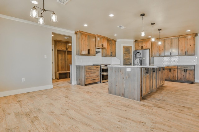 kitchen with pendant lighting, light wood-type flooring, an island with sink, and appliances with stainless steel finishes