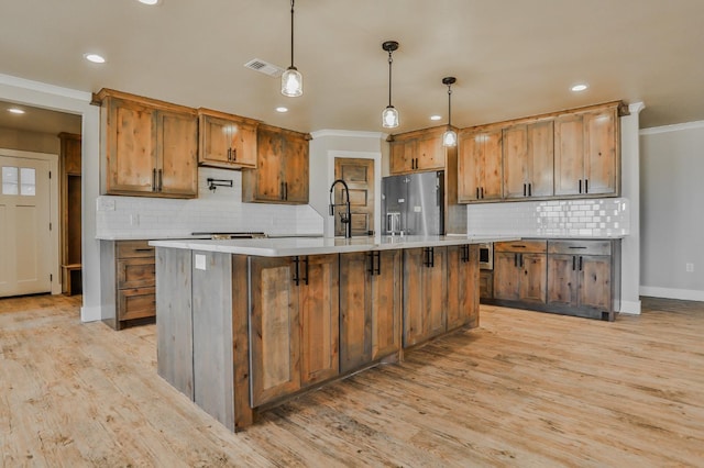 kitchen with hanging light fixtures, stainless steel refrigerator with ice dispenser, an island with sink, and light hardwood / wood-style floors