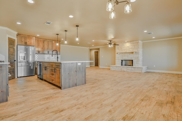 kitchen featuring a stone fireplace, hanging light fixtures, a center island with sink, stainless steel appliances, and backsplash