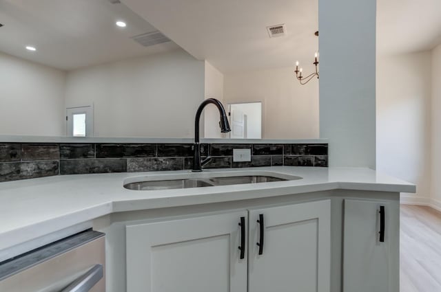 kitchen with sink, stainless steel dishwasher, kitchen peninsula, light hardwood / wood-style floors, and white cabinets