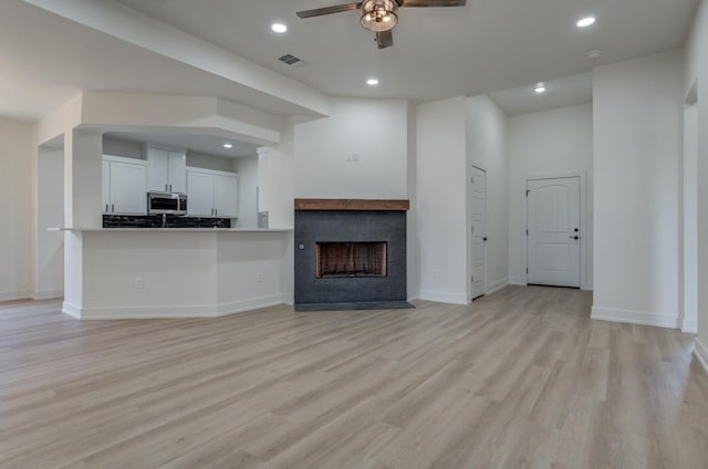 unfurnished living room with ceiling fan, a fireplace, and light hardwood / wood-style flooring