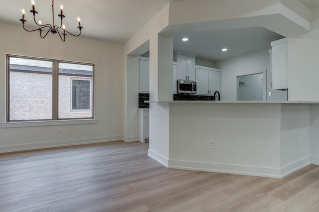 kitchen with white cabinets, hanging light fixtures, kitchen peninsula, an inviting chandelier, and light hardwood / wood-style flooring