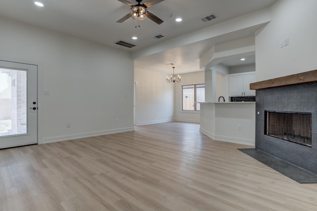 unfurnished living room featuring a tiled fireplace, ceiling fan with notable chandelier, and light hardwood / wood-style flooring