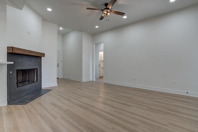 unfurnished living room with ceiling fan, a tiled fireplace, and light hardwood / wood-style flooring