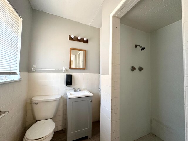 bathroom featuring walk in shower, vanity, toilet, and tile walls