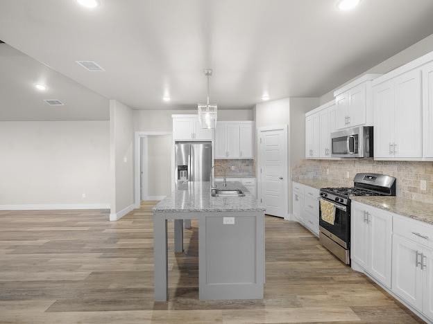 kitchen with white cabinetry, stainless steel appliances, tasteful backsplash, and a center island with sink