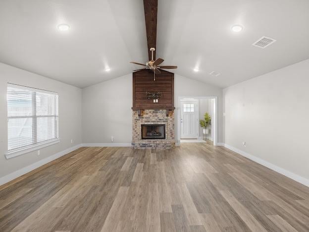 unfurnished living room featuring a fireplace, lofted ceiling with beams, light hardwood / wood-style flooring, and a wealth of natural light