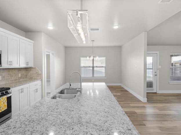 kitchen featuring sink, stainless steel range, pendant lighting, light stone countertops, and white cabinets