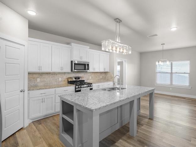 kitchen with sink, appliances with stainless steel finishes, a kitchen island with sink, white cabinets, and decorative light fixtures