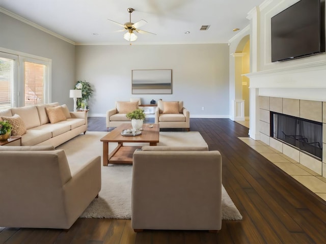 living room with crown molding, ceiling fan, dark hardwood / wood-style floors, and a tile fireplace