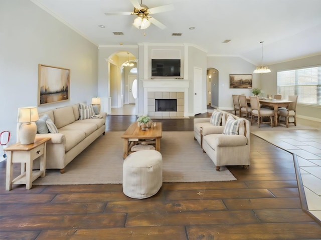 living room featuring crown molding, dark wood-type flooring, a tile fireplace, ceiling fan with notable chandelier, and vaulted ceiling