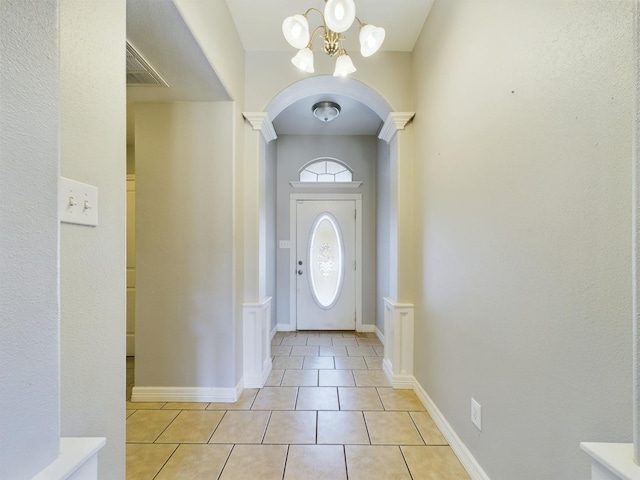 tiled foyer entrance with decorative columns and a chandelier