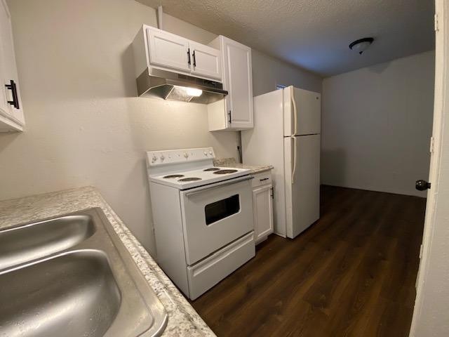 kitchen featuring white cabinetry, sink, dark hardwood / wood-style flooring, white appliances, and a textured ceiling