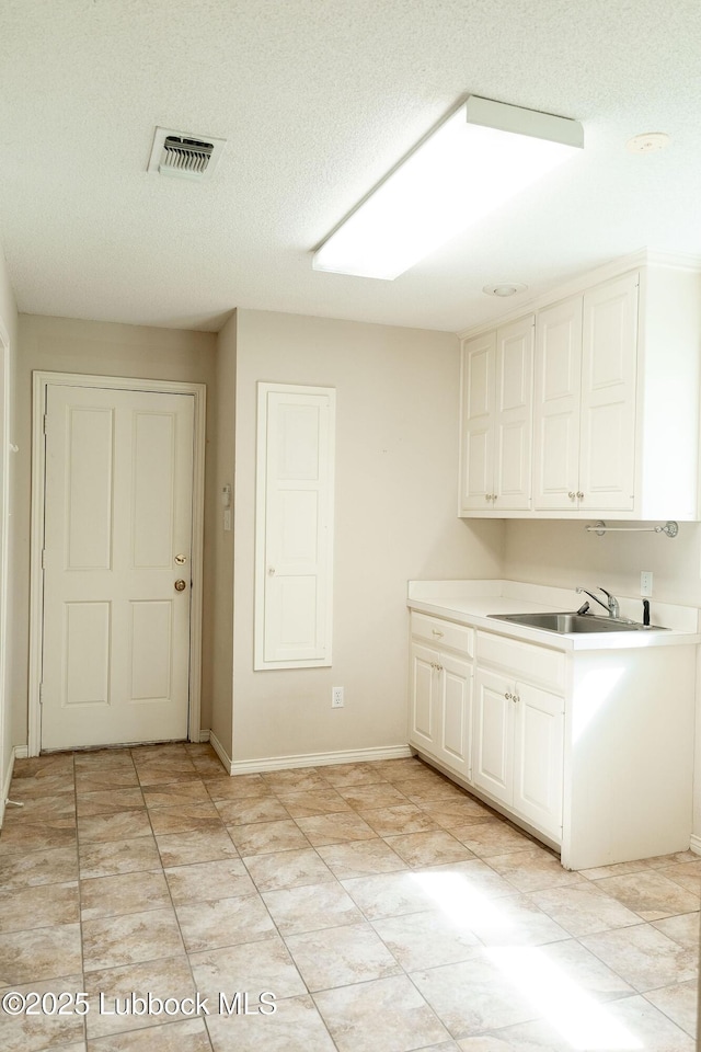4420 87th St, Lubbock, TX 79424 - kitchen with white cabinetry, a sink, light countertops, a textured ceiling, and baseboards