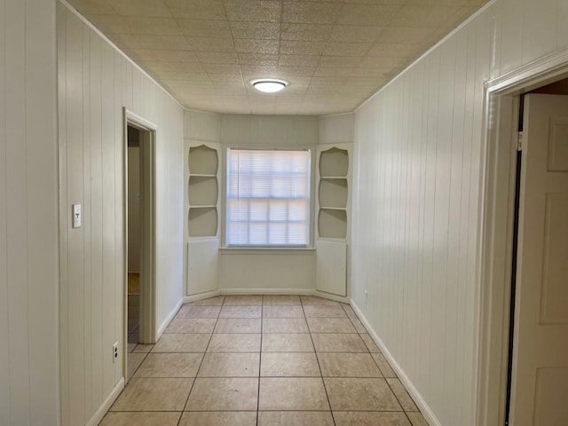 corridor with light tile patterned floors, built in features, and wooden walls