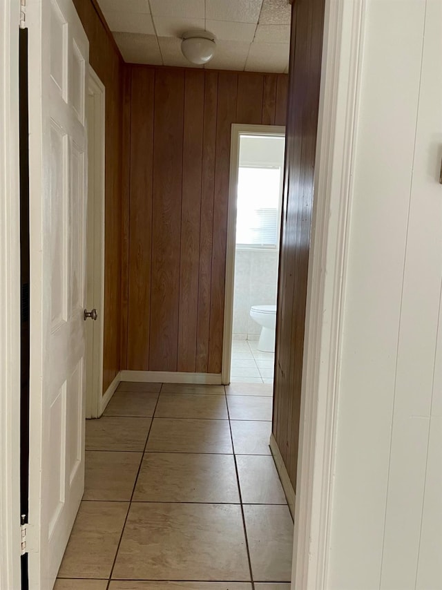 hallway featuring a drop ceiling, light tile patterned floors, and wood walls