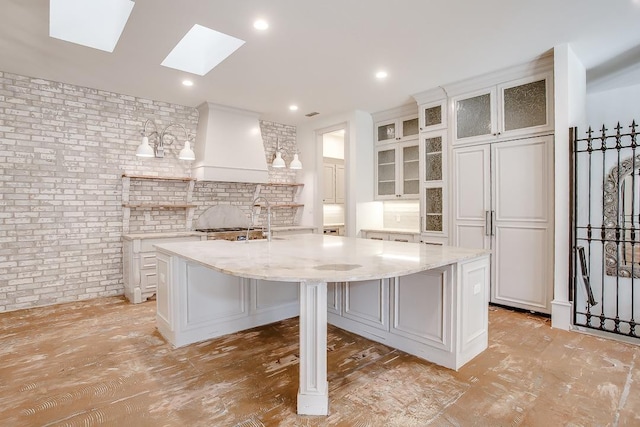 kitchen featuring white cabinetry, premium range hood, light stone countertops, and a kitchen island with sink