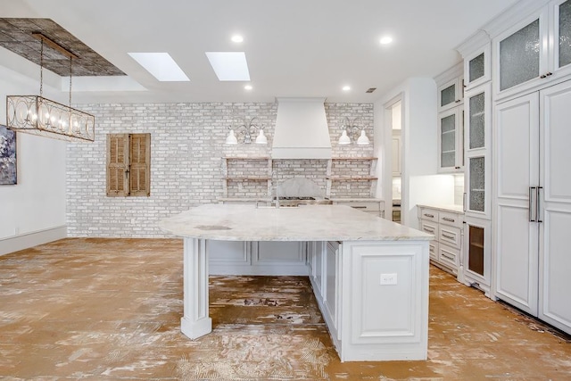 kitchen featuring a kitchen island with sink, white cabinetry, a kitchen breakfast bar, light stone counters, and brick wall