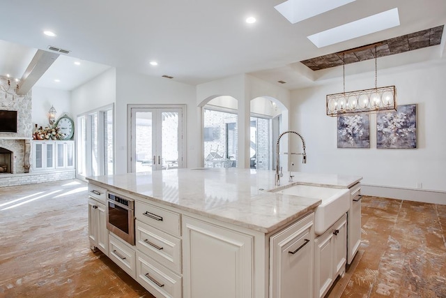 kitchen with sink, light stone counters, a fireplace, oven, and a kitchen island with sink